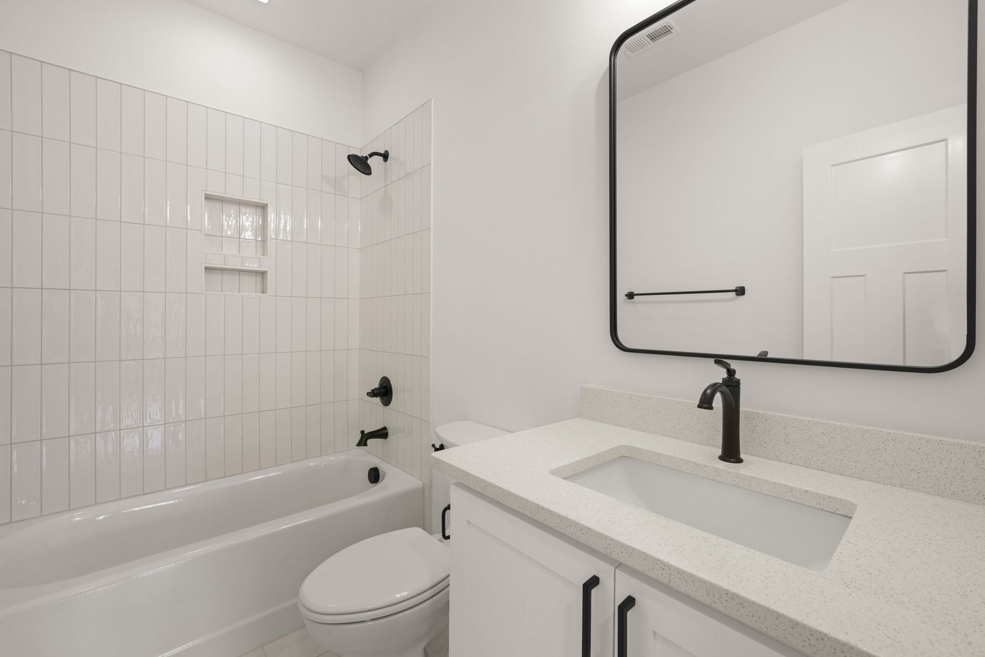 Bright bathroom with white tile, bathtub, vanity, and large mirror