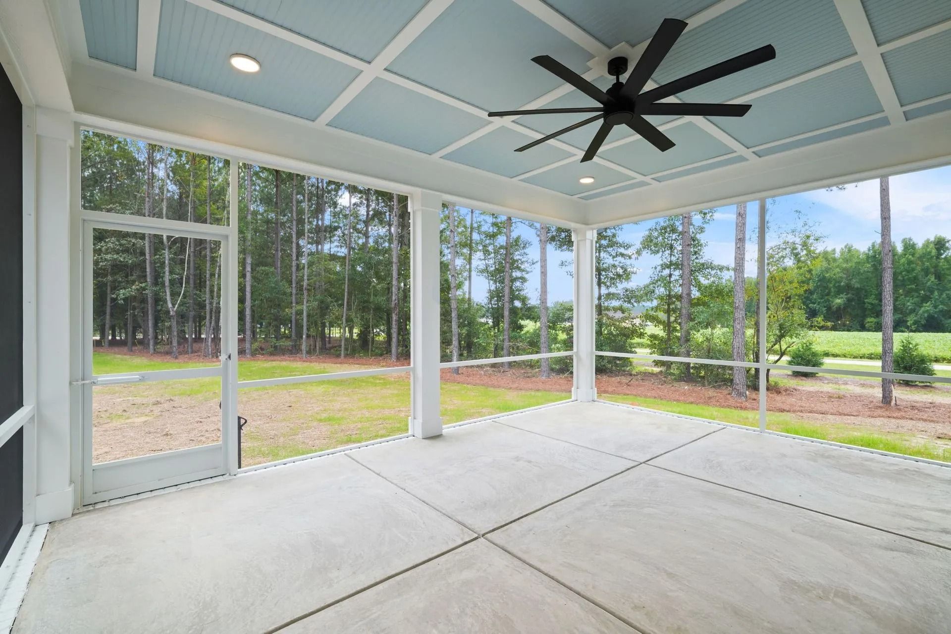 Covered screened porch with concrete floor, white framing, ceiling fan, and view of trees and lawn outside