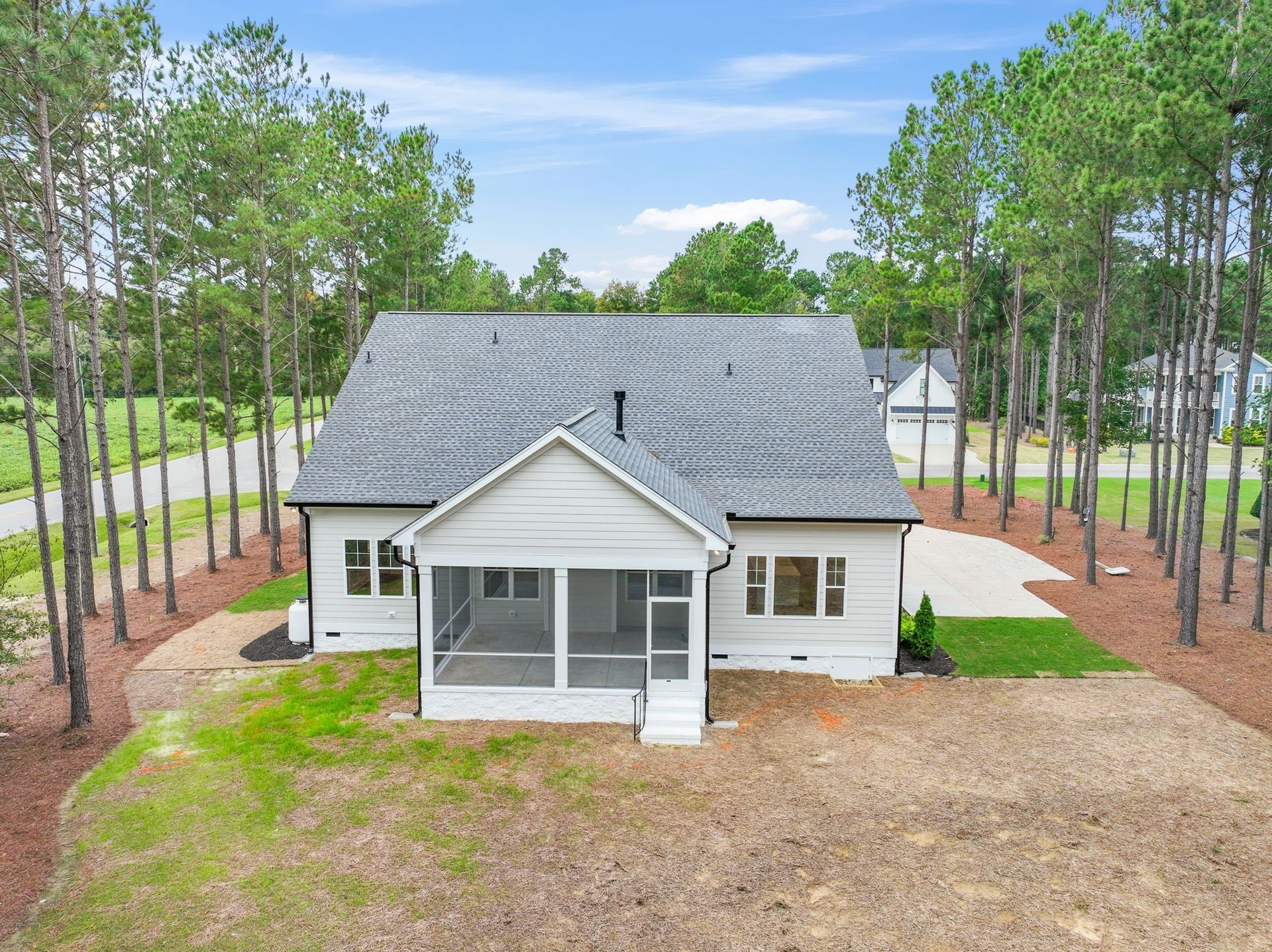 Gray house with screened front porch, white trim, and pine trees surrounding the yard