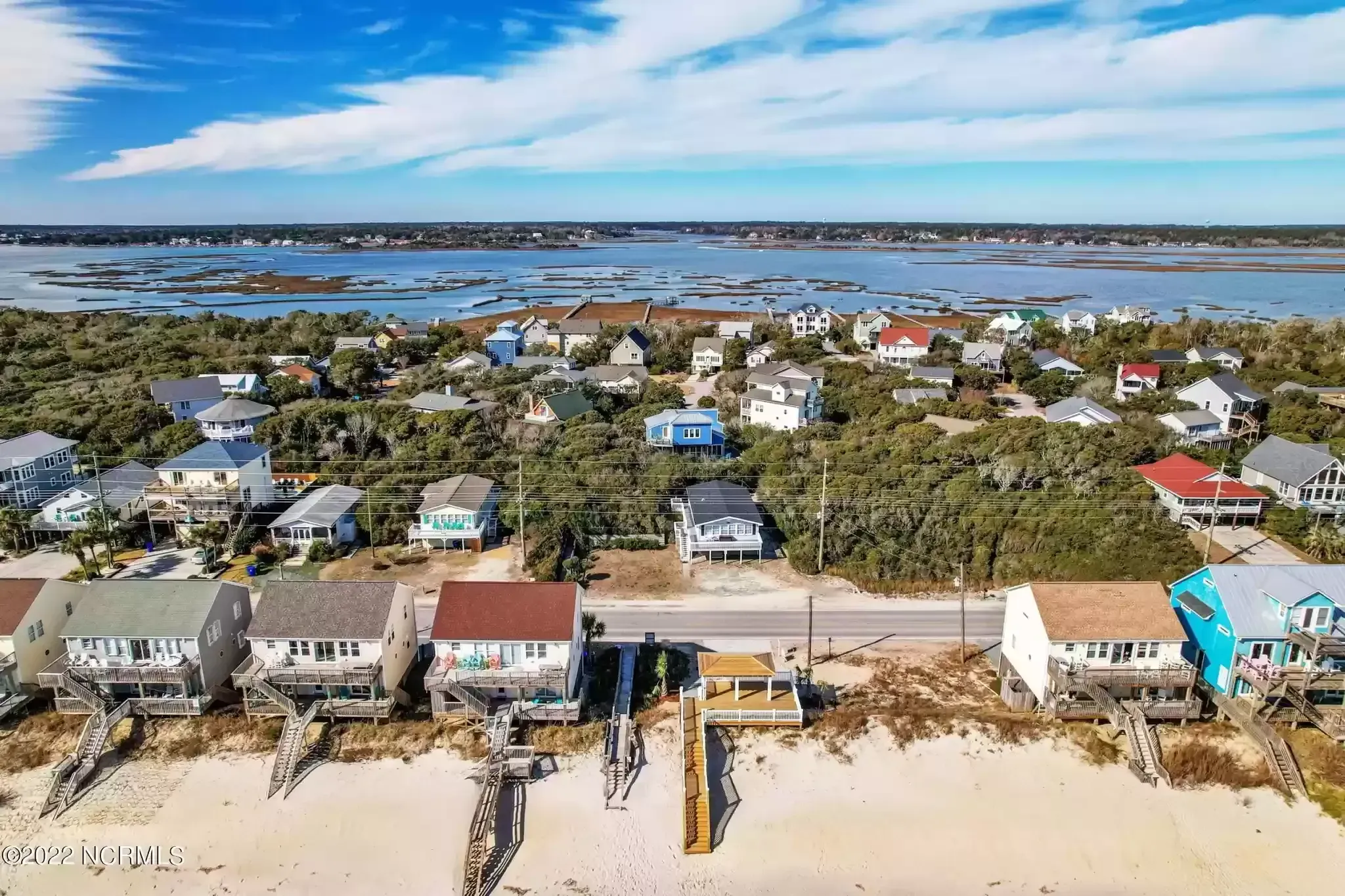 Aerial view of colorful beach houses along a sandy shoreline with water and marshland beyond