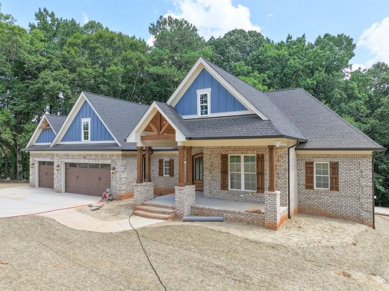 New brick and stone suburban house with blue gables and a three-car garage on a wooded lot