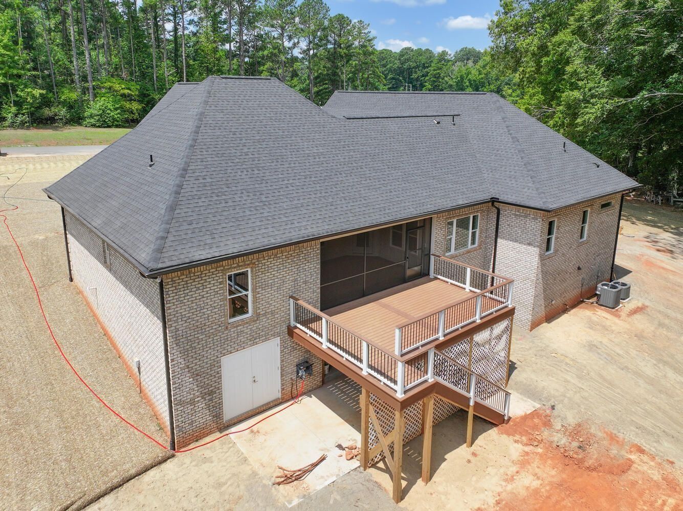 Aerial view of a new brick house with a gray roof and front porch in a wooded lot