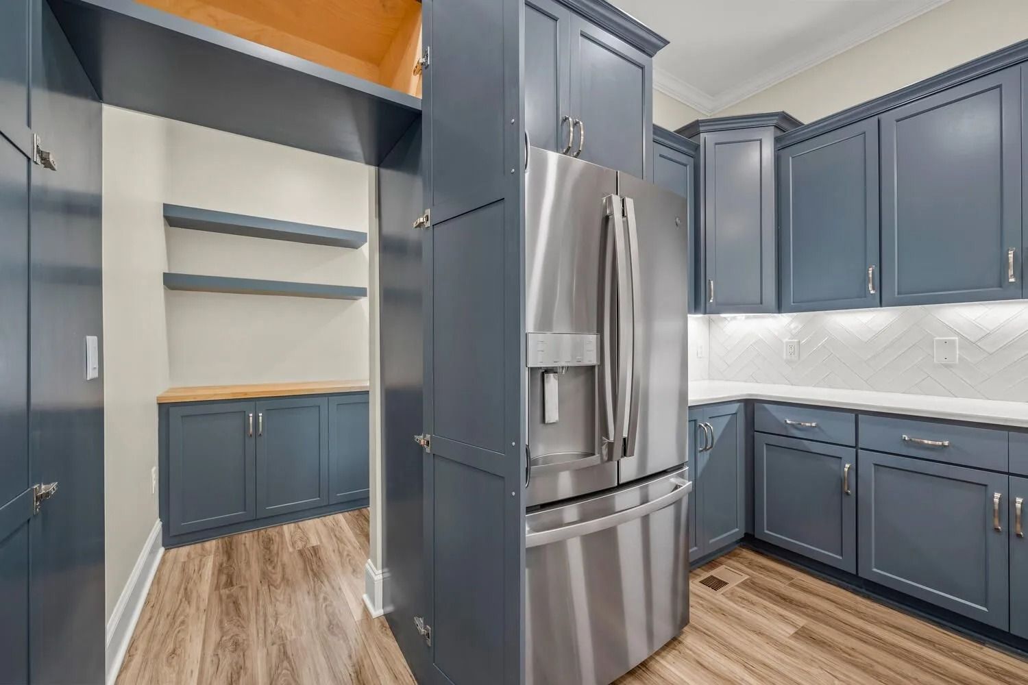 Modern kitchen with navy cabinets, stainless steel refrigerator, and wood flooring