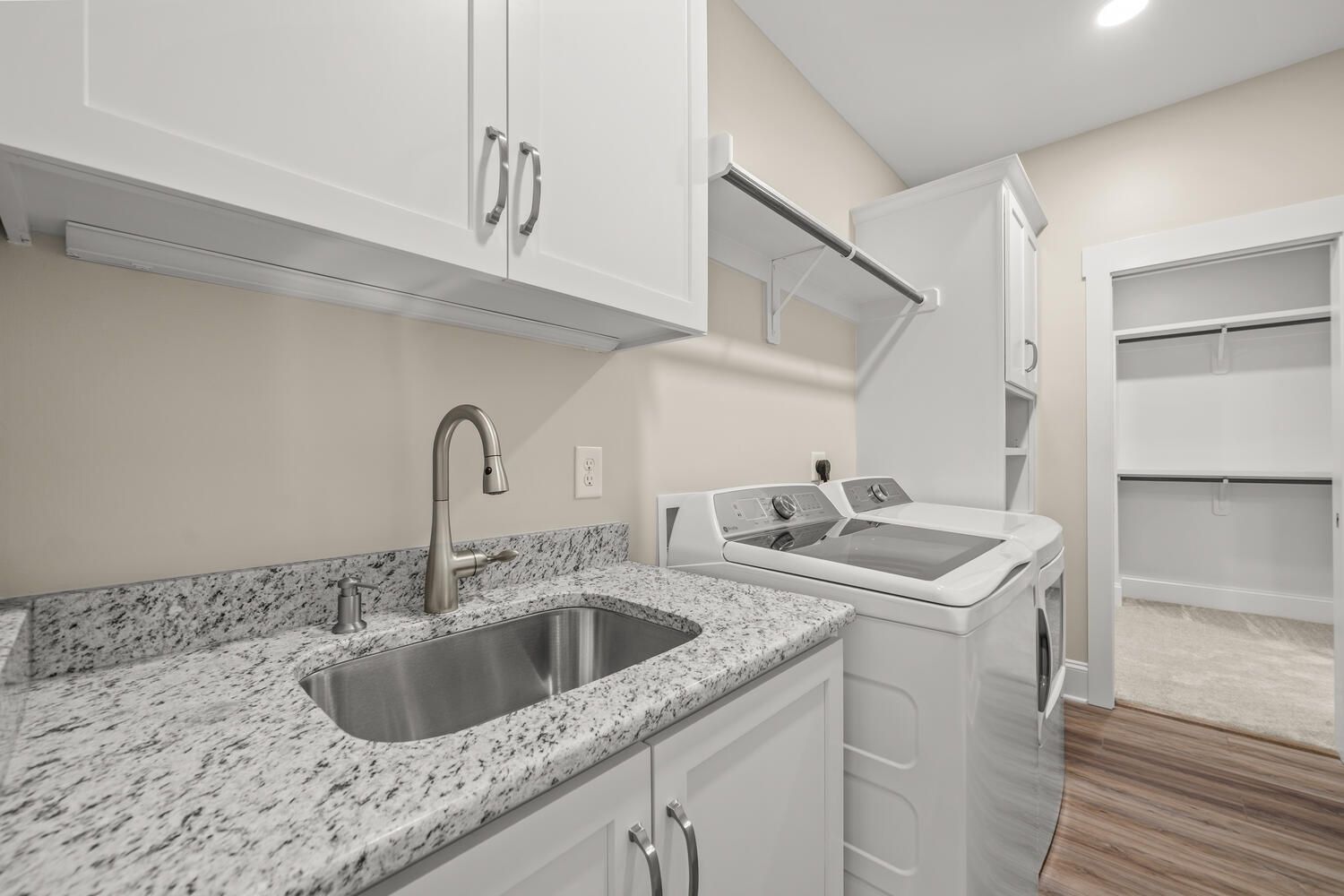 Bright laundry room with sink, washer, white cabinets, and open shelving.
