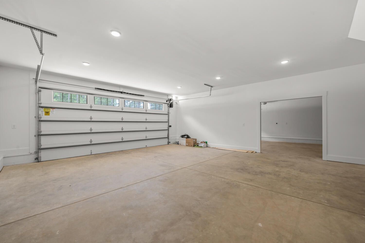 Empty unfinished garage with concrete floor, white walls, and a wide overhead door.