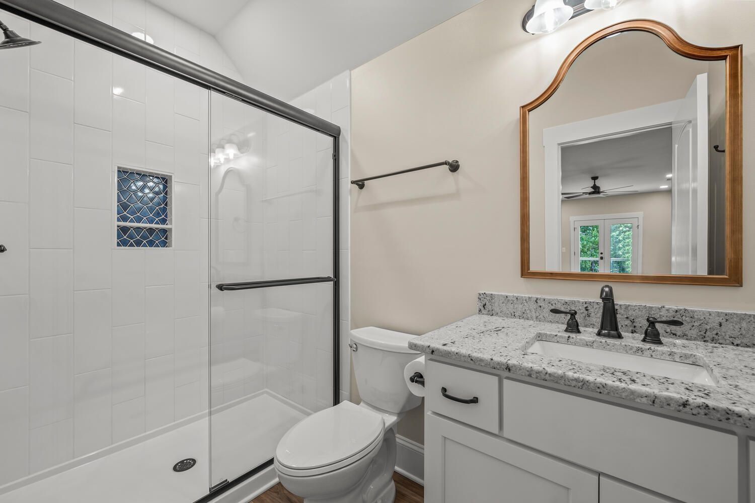 Modern bathroom with glass shower, toilet, and white vanity with granite countertop and wood-framed mirror