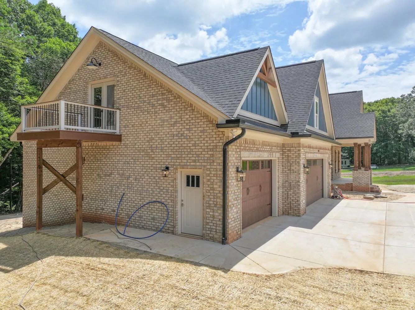 New brick house with double garage, balcony, and gravel driveway on a sunny day