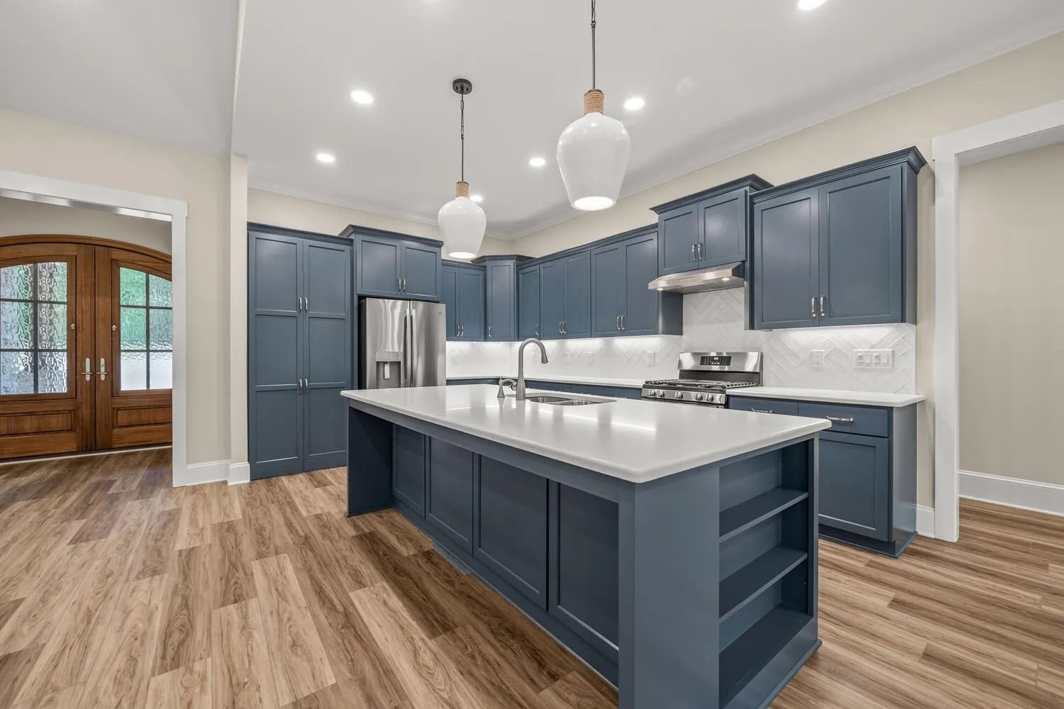 Modern kitchen with navy cabinets, large island, pendant lights, and wood floors