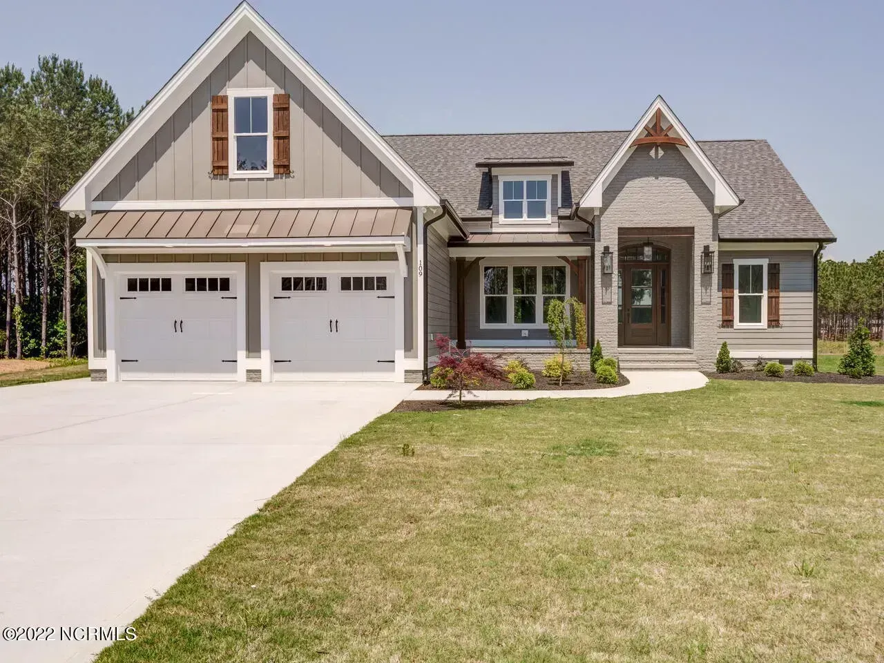 Suburban house with two-car garage, front porch, and a large lawn under a clear sky
