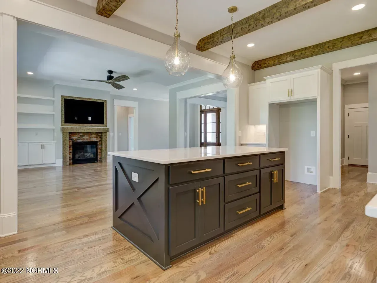 Modern open-concept kitchen with a dark island, hardwood floors, white cabinets, and exposed ceiling beams