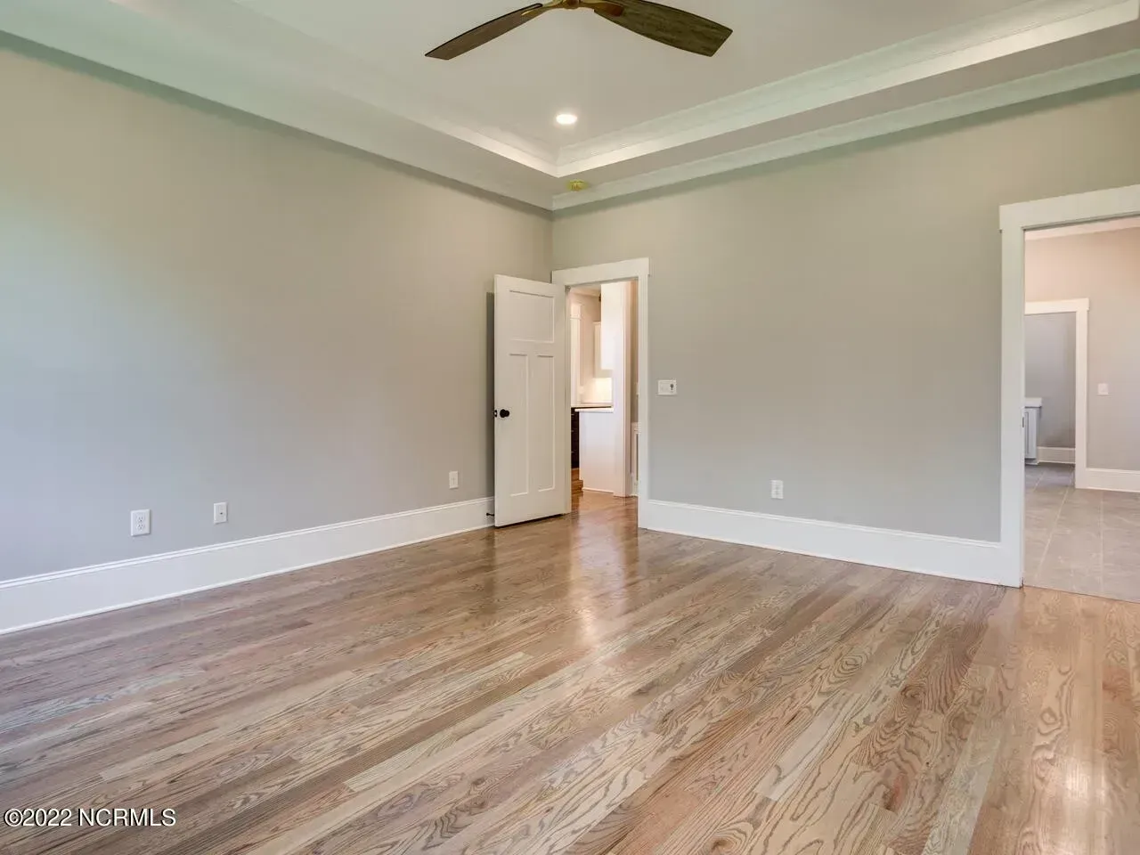 Empty living room with hardwood floors, gray walls, ceiling fan, and doorways to adjacent rooms