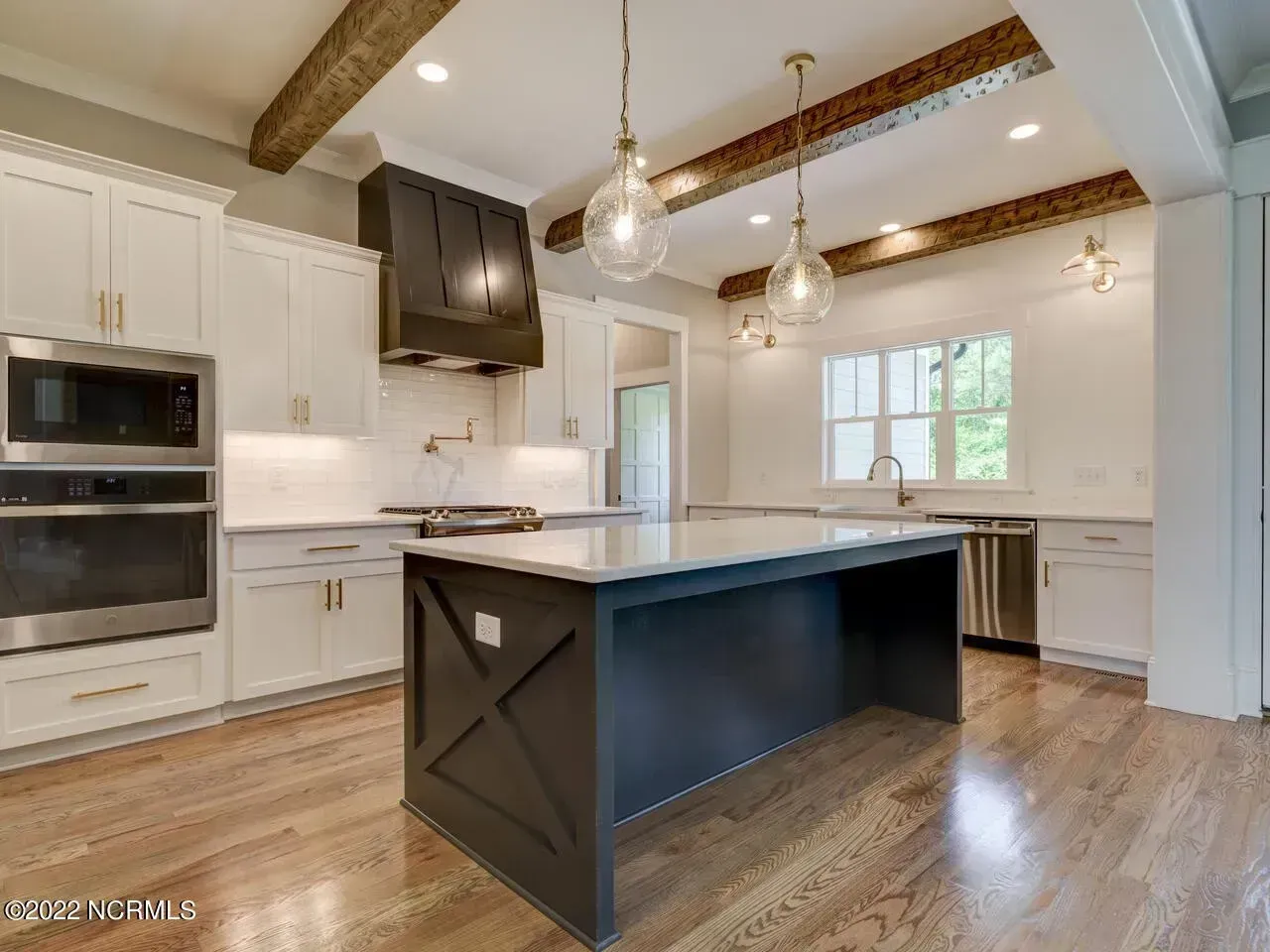 Bright modern kitchen with white cabinets, dark island, wood beams, and hardwood floors