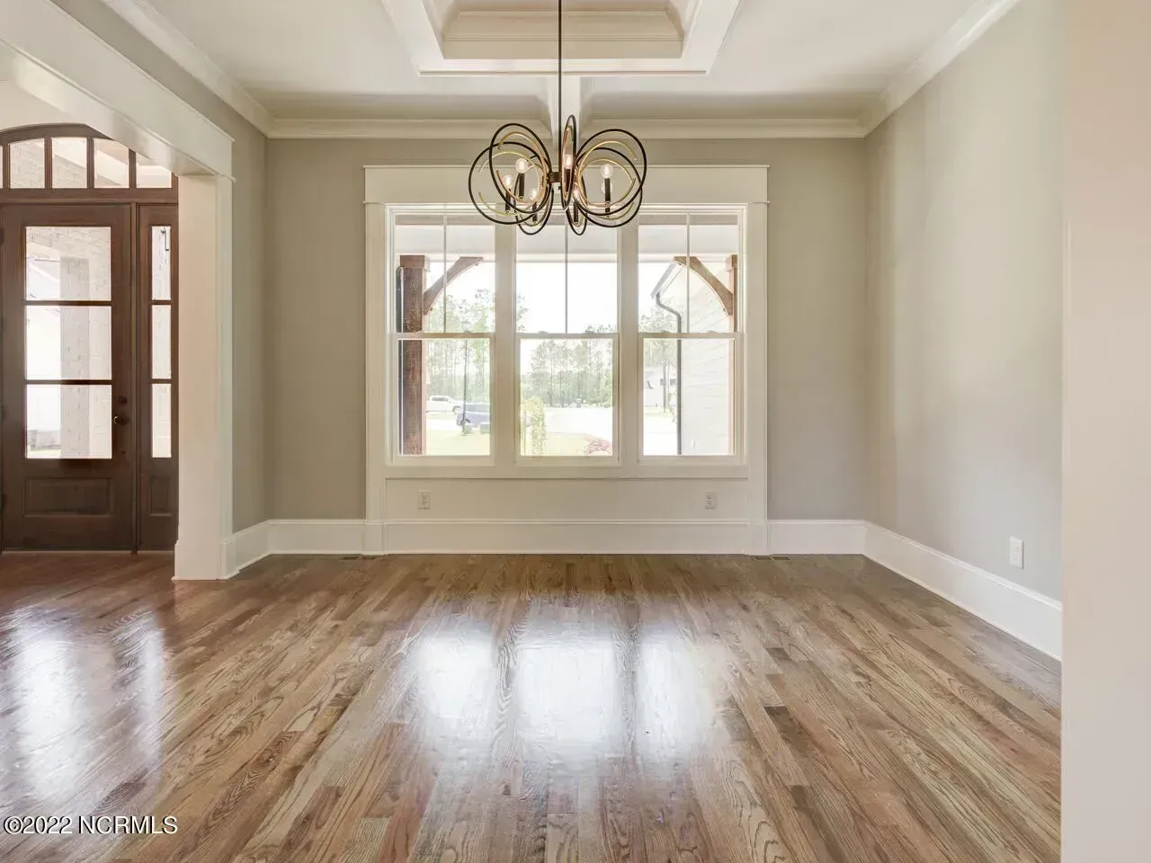 Empty dining room with hardwood floors, chandelier, and large windows beside a front door