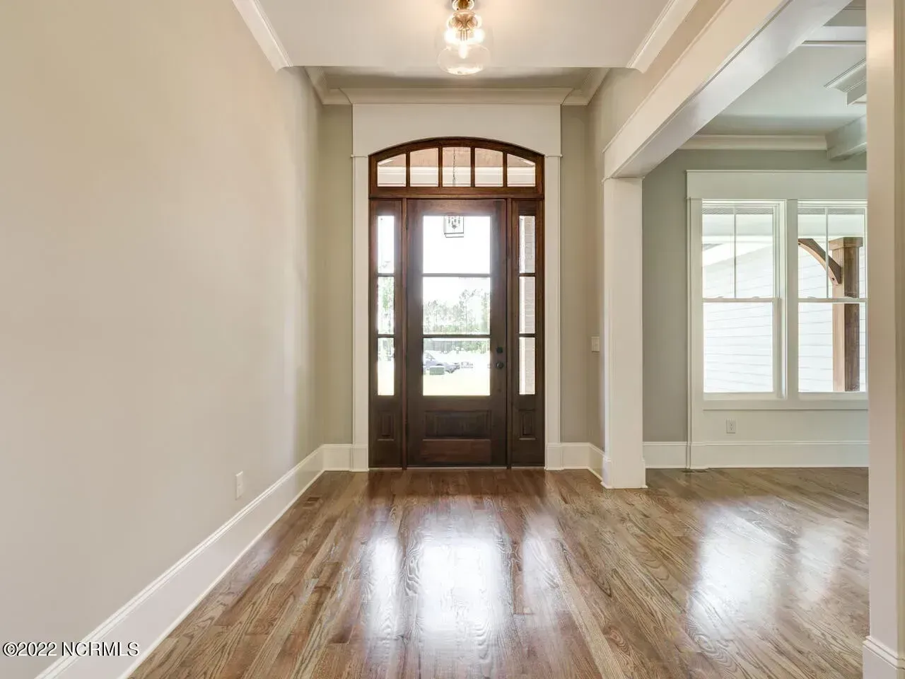 Empty hallway with polished wood floors, white walls, and a dark front door with sidelights