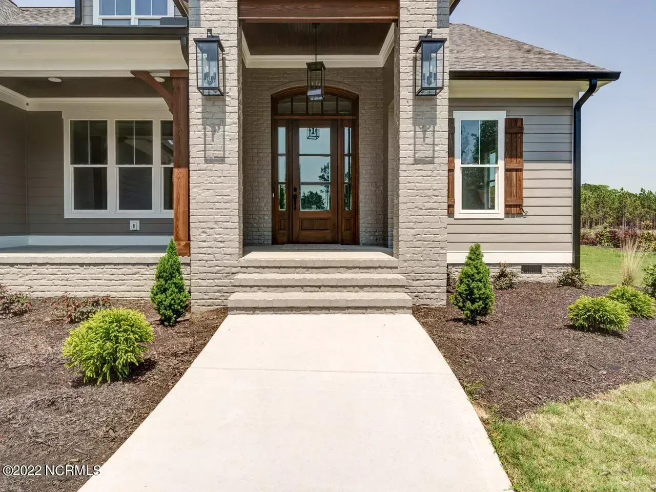 Front entrance of a modern brick house with a concrete walkway and landscaped front yard