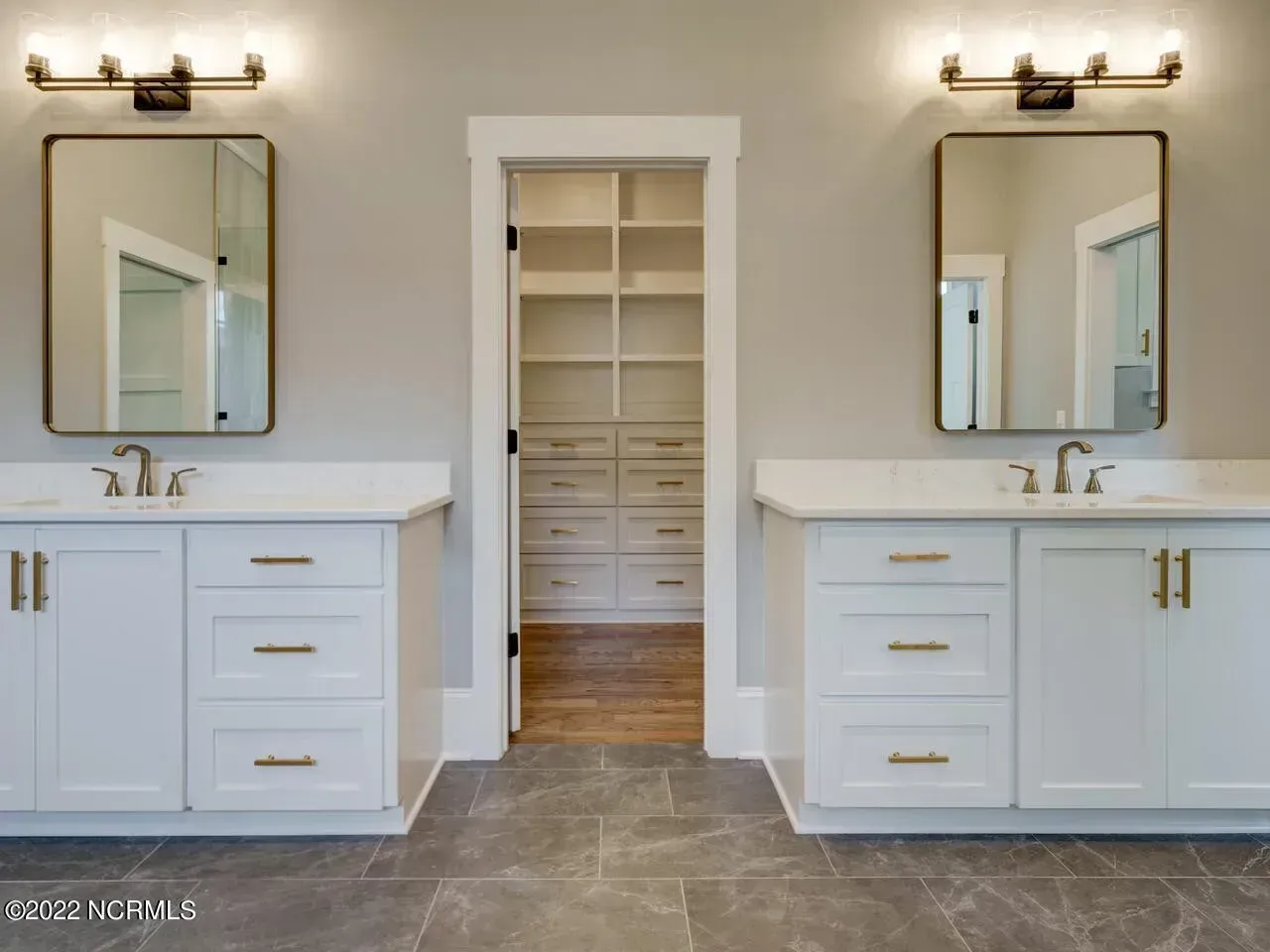 Bright double bathroom vanity with mirrors, brass fixtures, and a central walk-in closet doorway