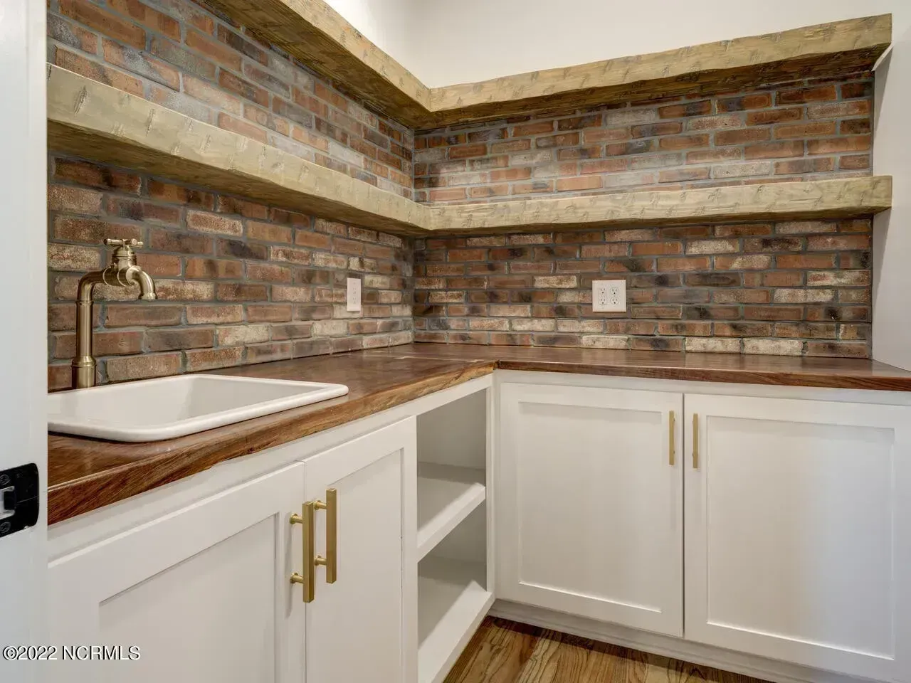 Compact kitchen corner with brick backsplash, white cabinets, and a farmhouse sink