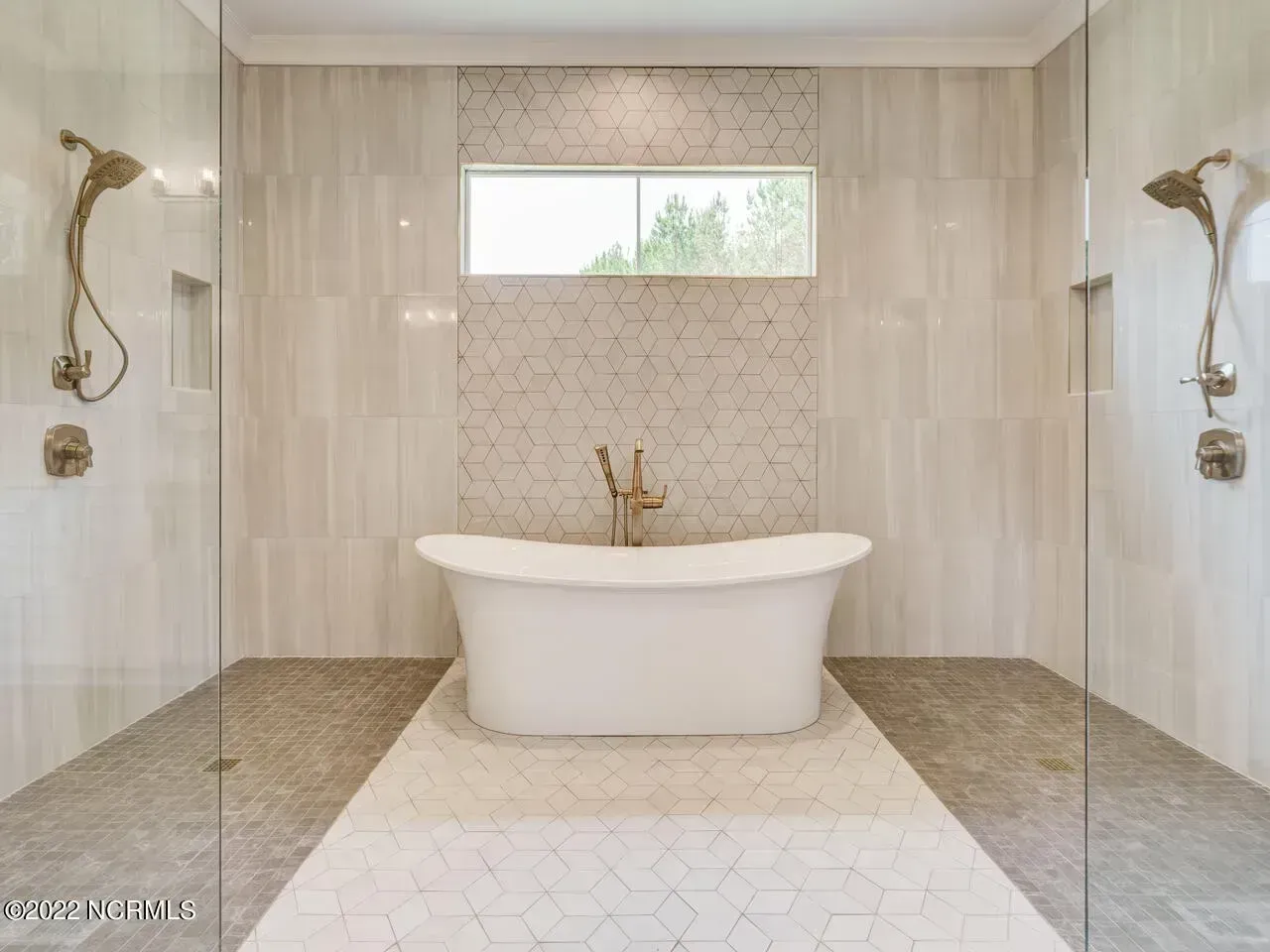 Bright marble bathroom with a freestanding tub, gold fixtures, and a small window above.