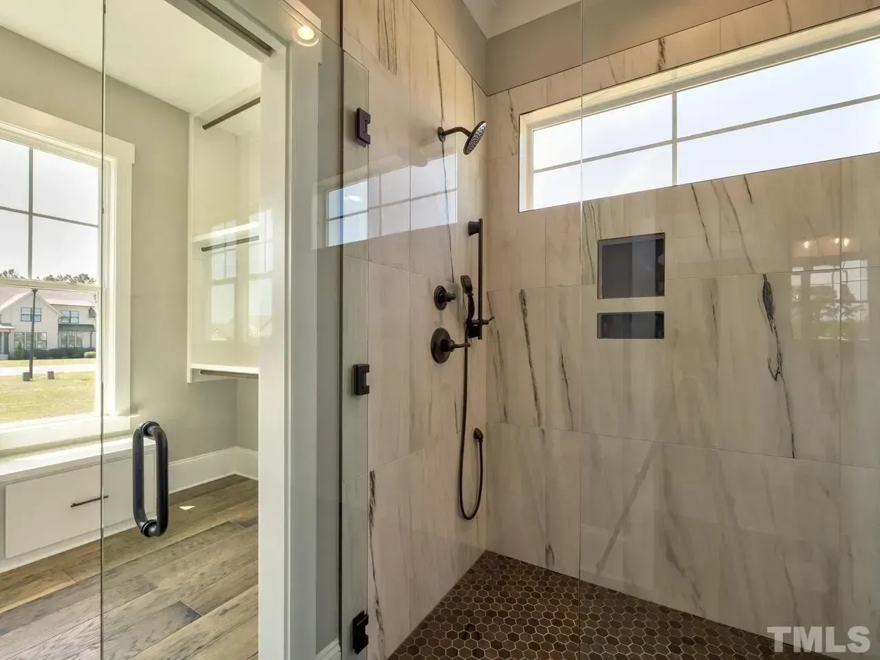 Walk-in shower with glass door, white marble walls, black fixtures, and pebble tile floor
