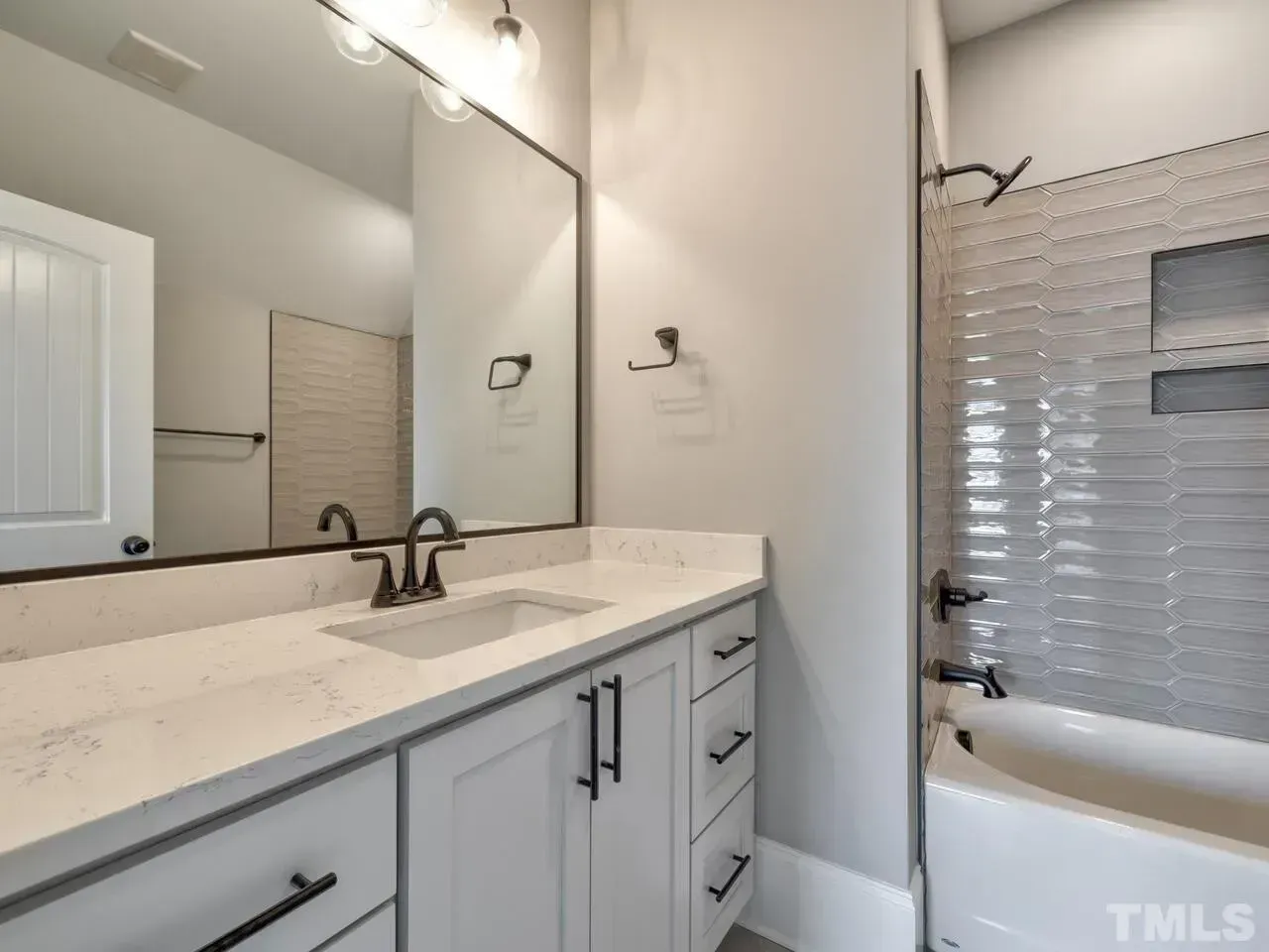 Modern bathroom vanity with large mirror, double sink, white cabinets, and tiled shower with glass door