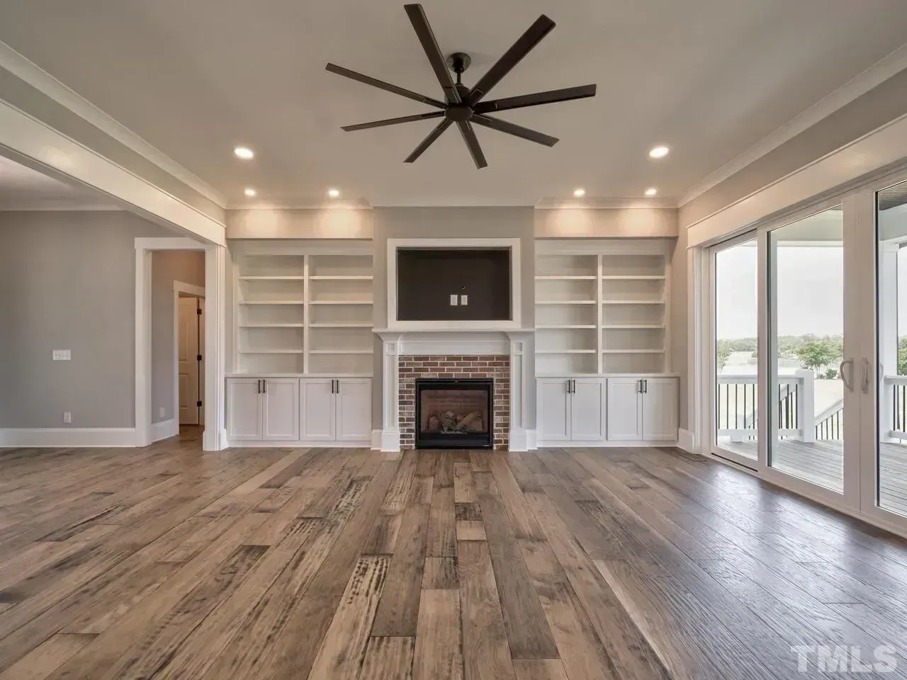 Spacious living room with built-in shelves, fireplace, wood floors, ceiling fan, and large windows.