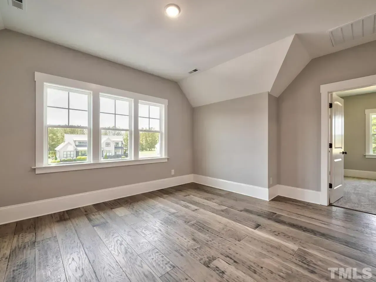 Empty bedroom with gray walls, wood floors, and three windows letting in daylight