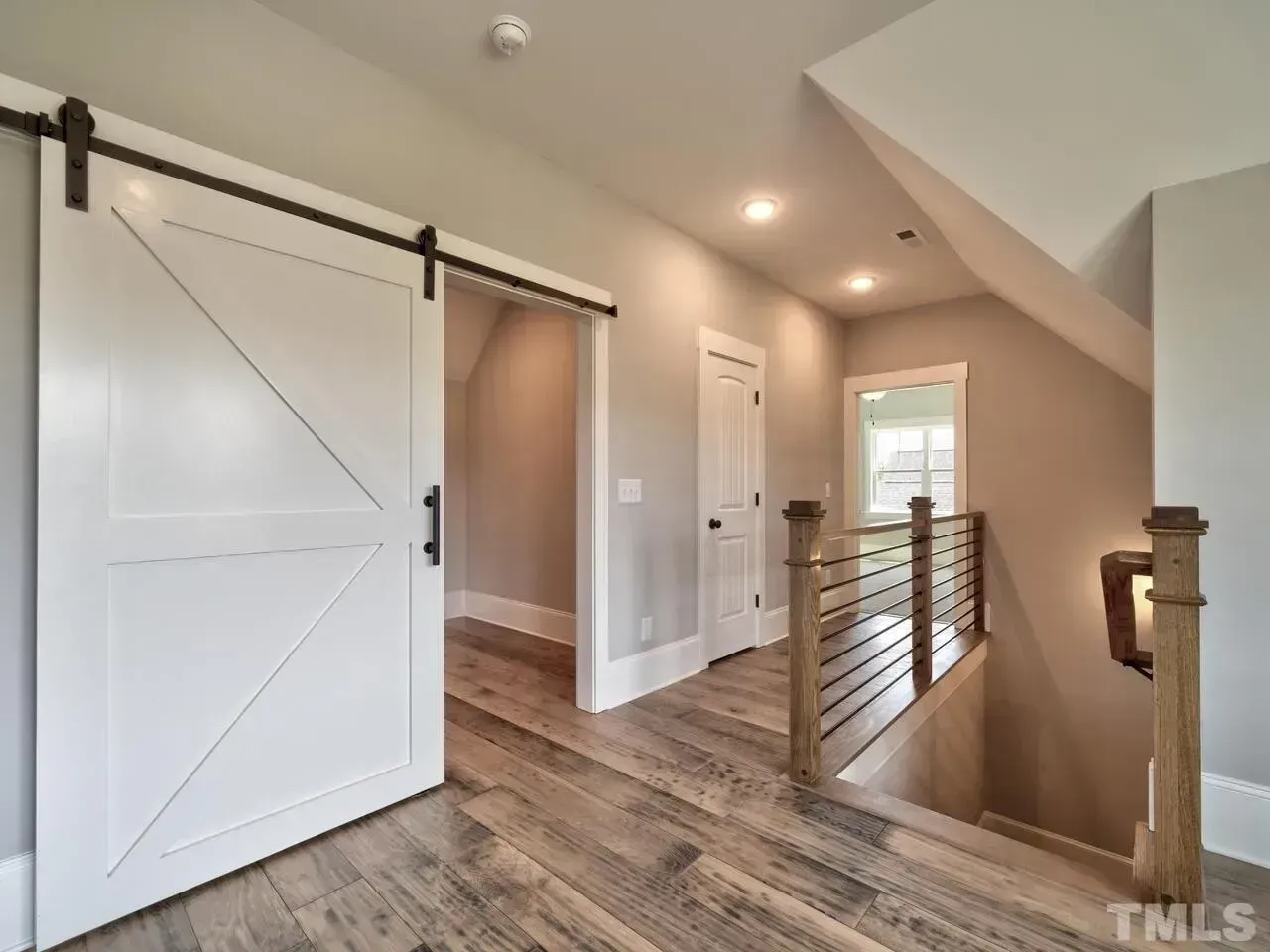 Bright upstairs hallway with sliding barn door, wood floors, railing, and recessed lights