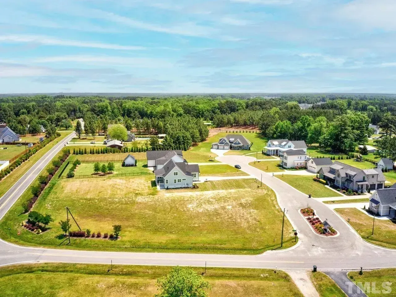 Aerial view of a suburban neighborhood with new houses, roads, and green trees under a clear sky