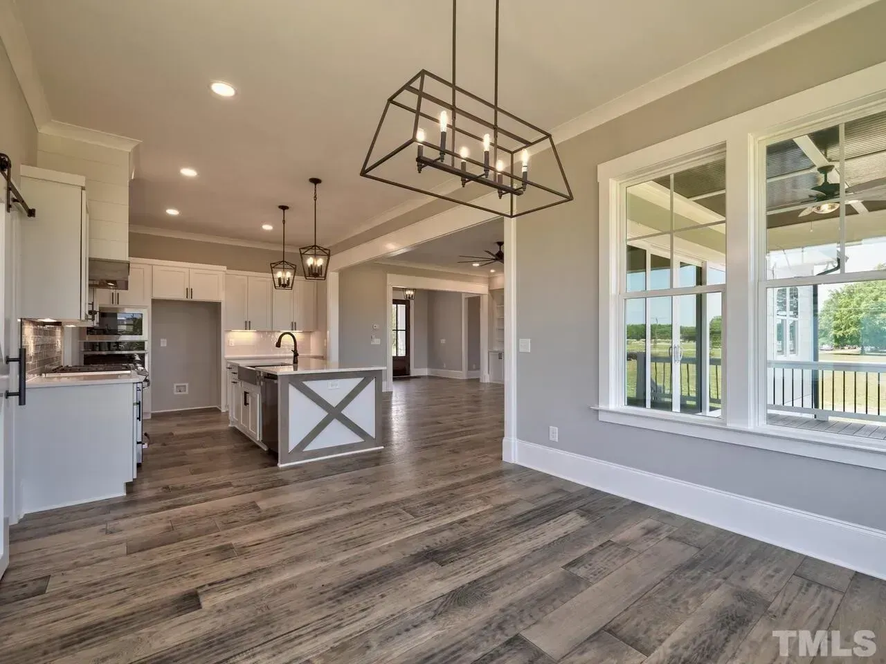 Bright open kitchen and dining area with gray wood floors, white walls, and large windows.