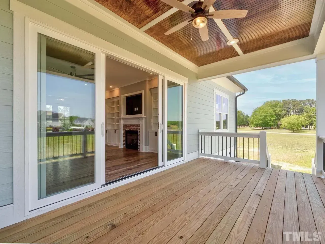 Covered wooden deck with white railings, sliding glass doors, and a ceiling fan overlooking a grassy yard