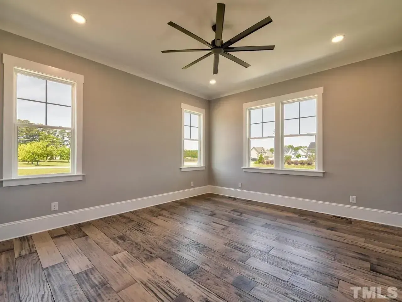 Empty room with hardwood floors, beige walls, and three windows under a ceiling fan