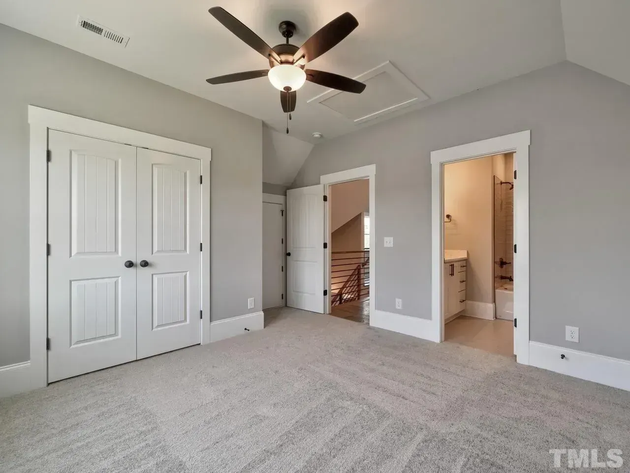 Empty carpeted bedroom with gray walls, ceiling fan, closet doors, and an open doorway to a bathroom and hallway