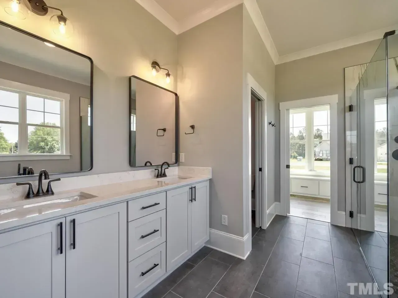 Modern bathroom with double vanity, large mirror, glass shower, and windowed nook with a freestanding tub
