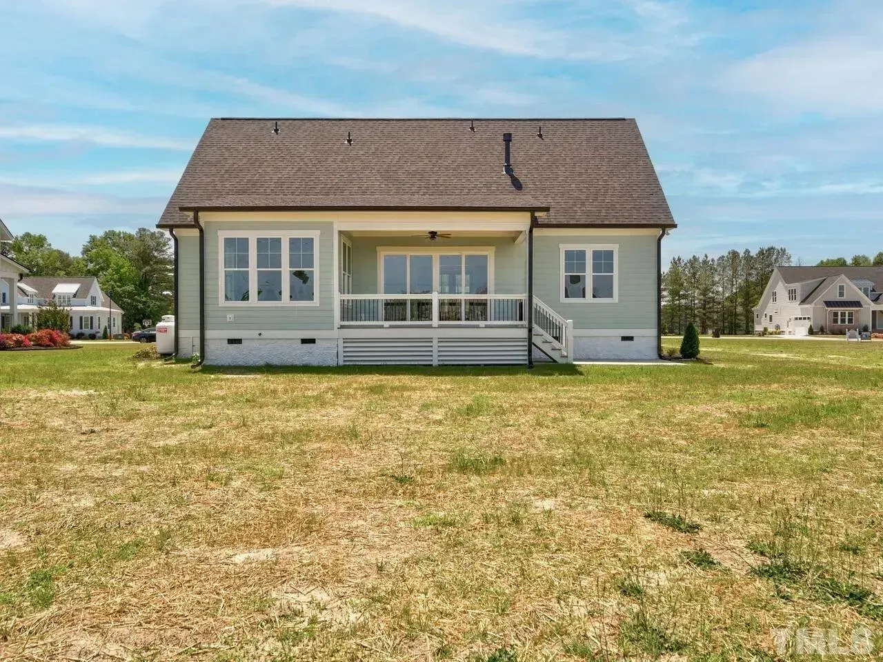 Single-story gray house with a front porch and large grassy yard under a blue sky