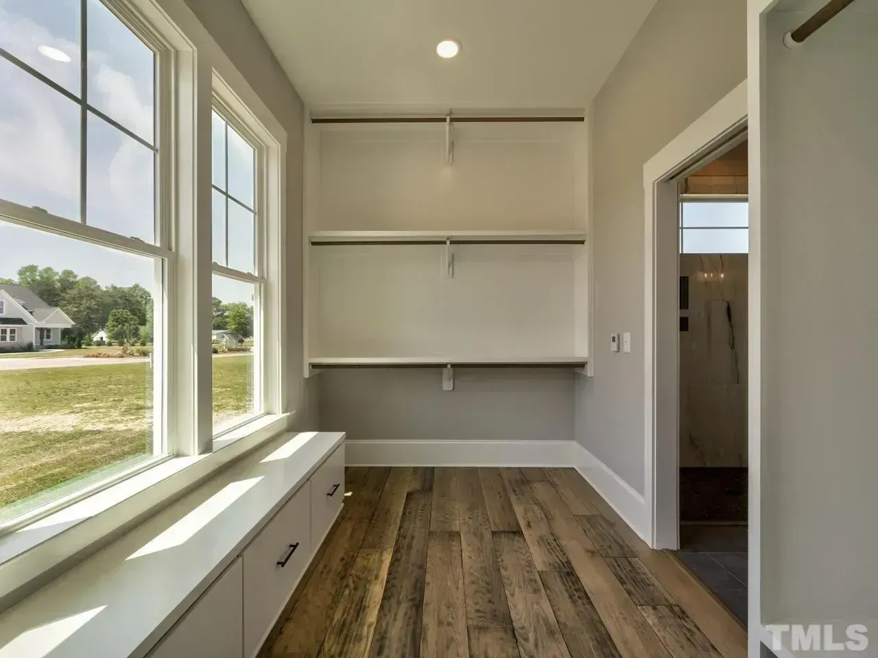 Bright empty walk-in closet with built-in shelves, gray walls, wood floor, and large window seating