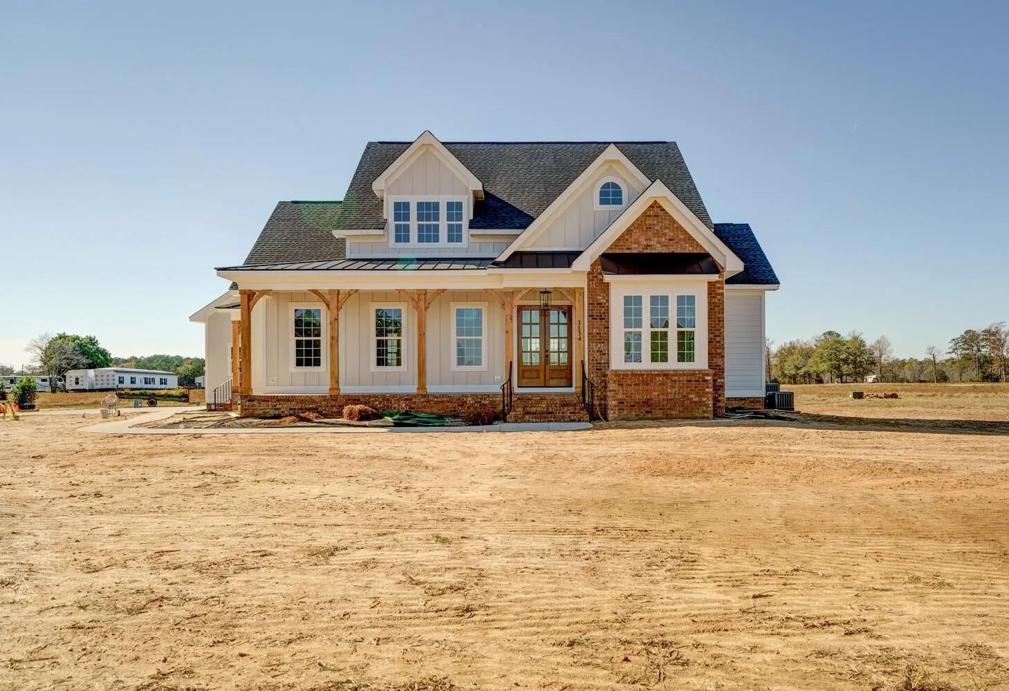 New beige house with dark roof on a bare lot under a clear sky