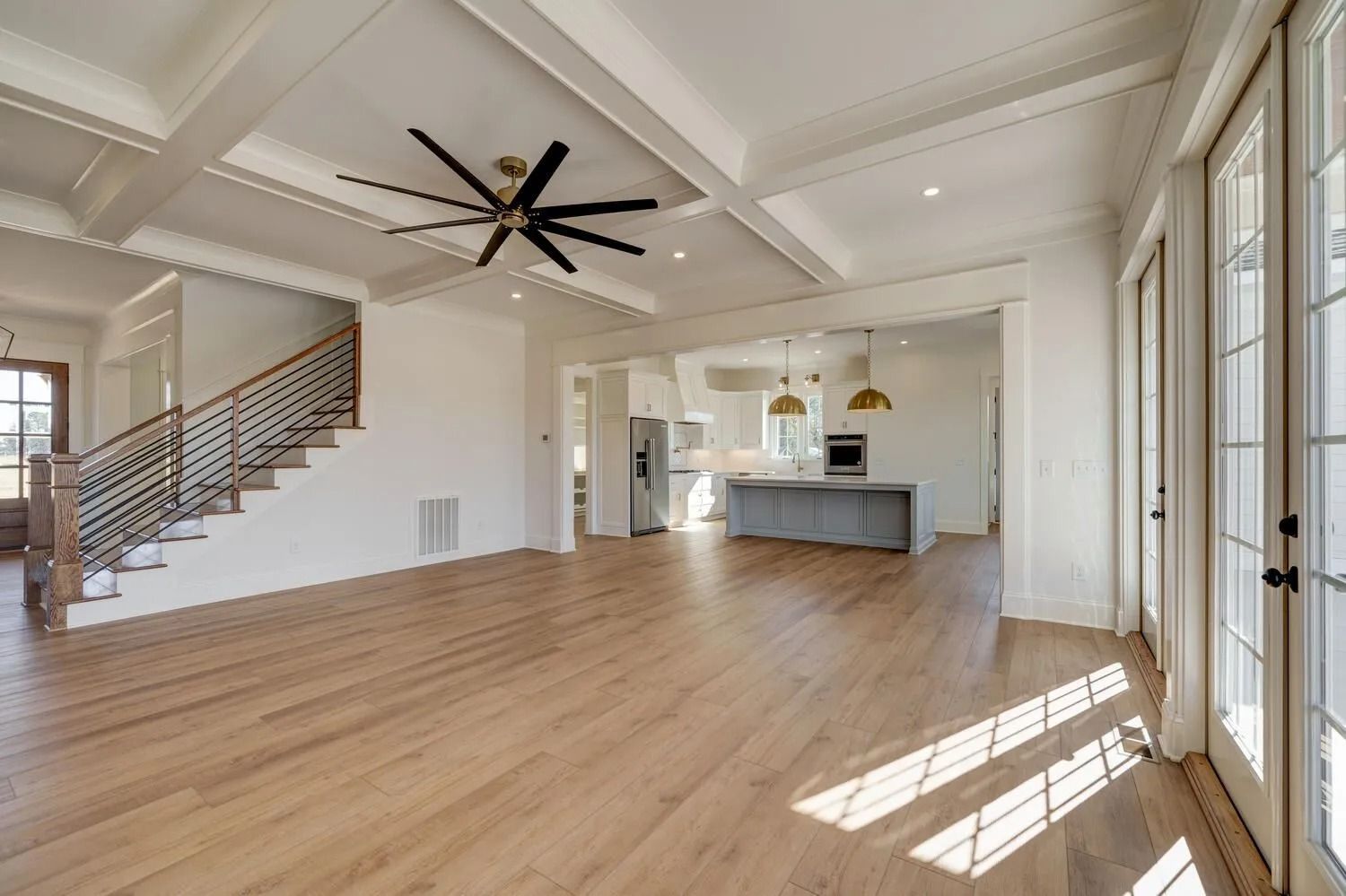 Spacious modern living room with wood floors, vaulted ceiling, staircase, and kitchen in the background