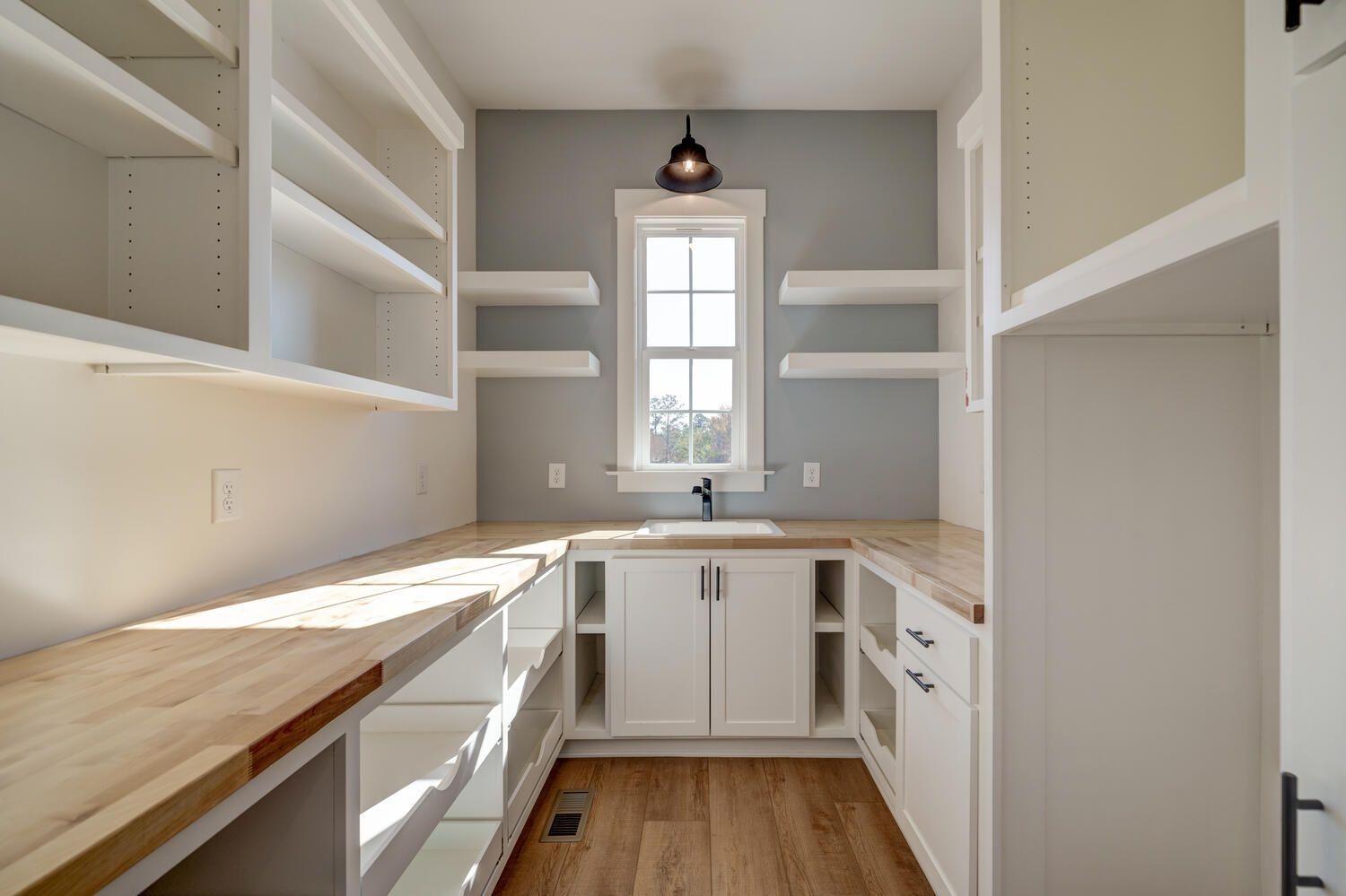 Bright white galley kitchen with open shelves, butcher-block counters, and a window over the sink.