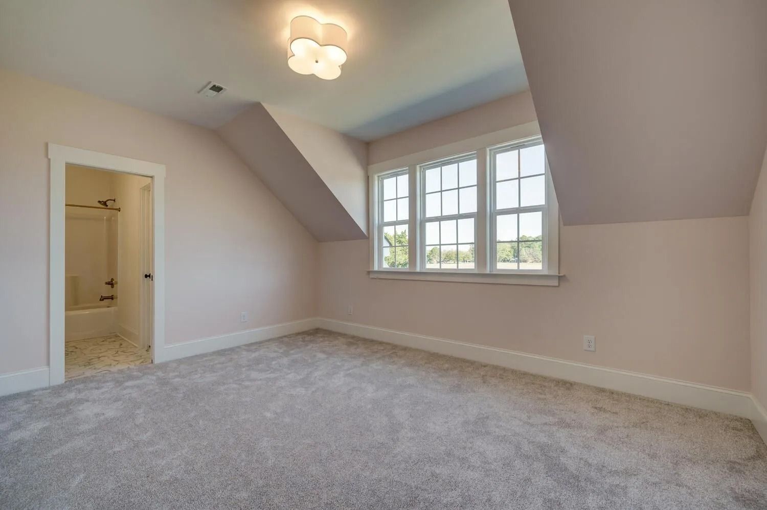 Empty beige bedroom with gray carpet, sloped ceiling, and a window with white trim.