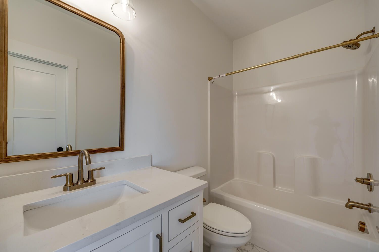 Bright white bathroom with vanity mirror, sink, toilet, and tub with gold fixtures