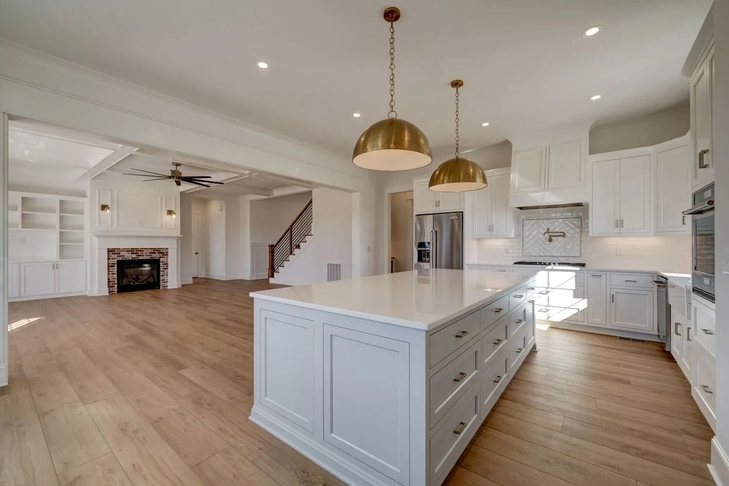 Bright modern kitchen with white cabinets, large island, brass pendant lights, and hardwood floors