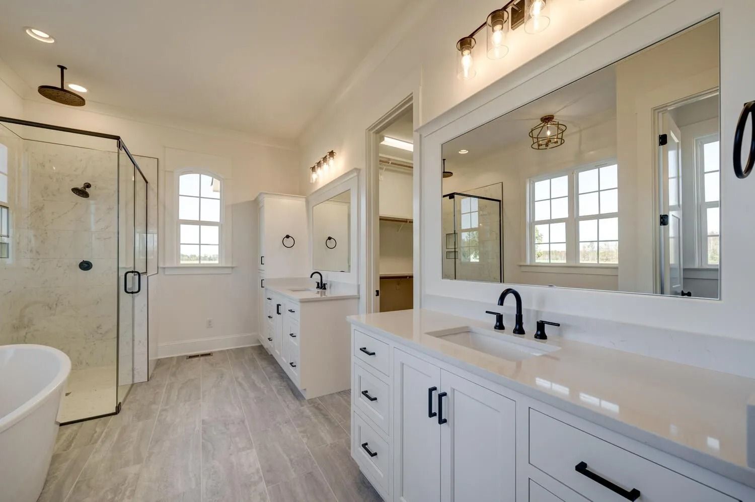 Bright white bathroom with double vanity, large mirror, bathtub, shower, and window