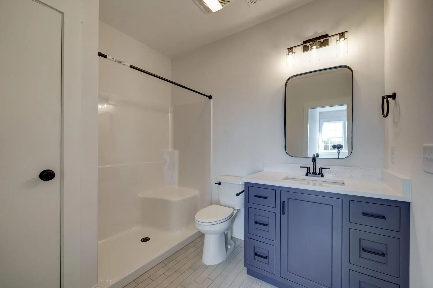 Bathroom with white walls, tub-shower, toilet, and blue vanity with mirror and sink.