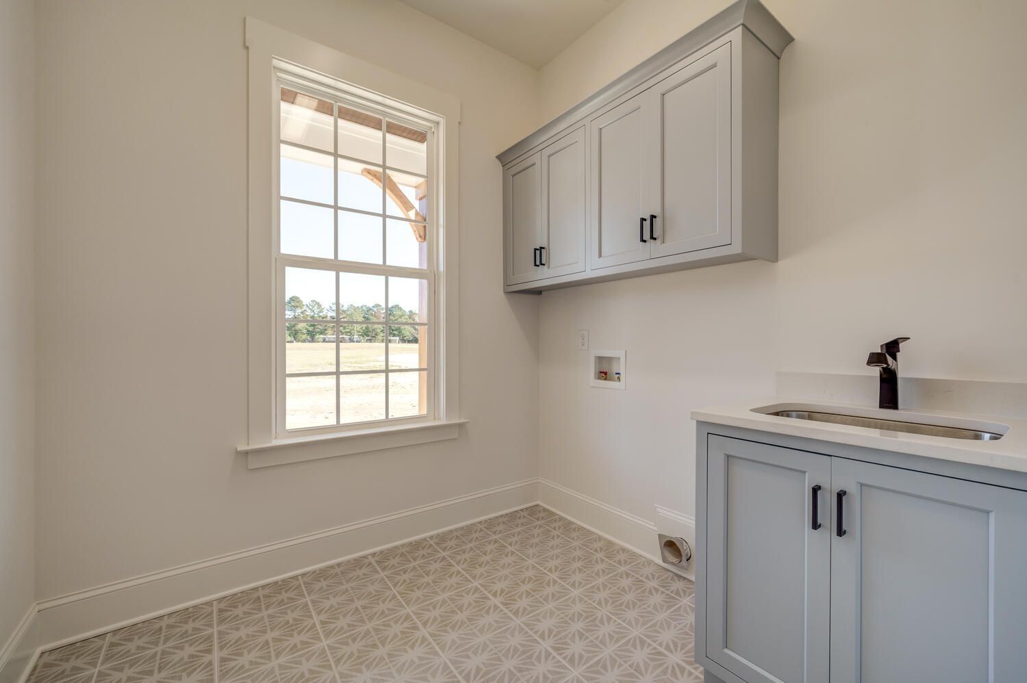 Empty laundry room with a window, white walls, and light gray cabinets and countertop.