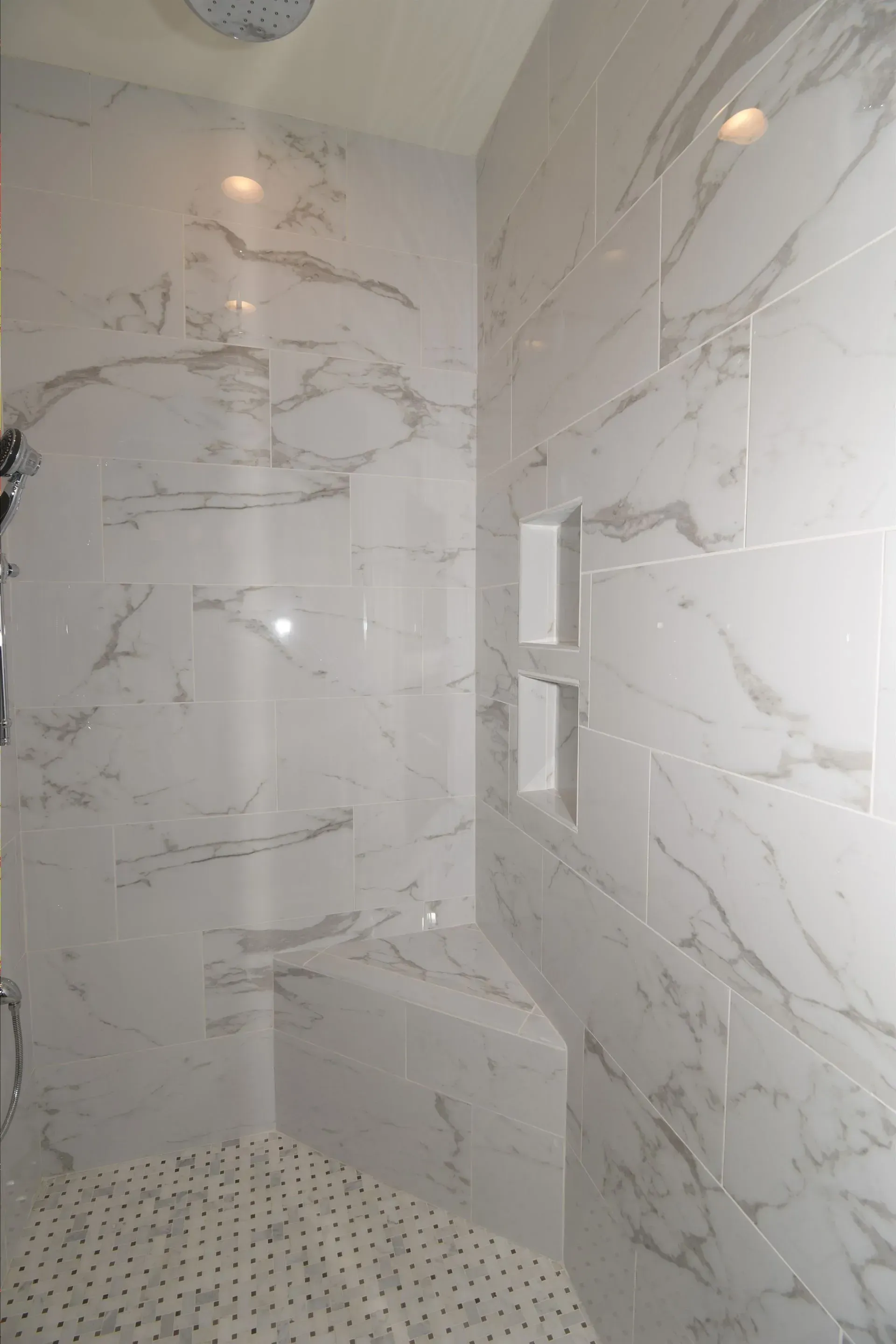 A shower with white marble-style wall tiles, a built-in corner bench, a recessed storage nook, and a tiled floor.