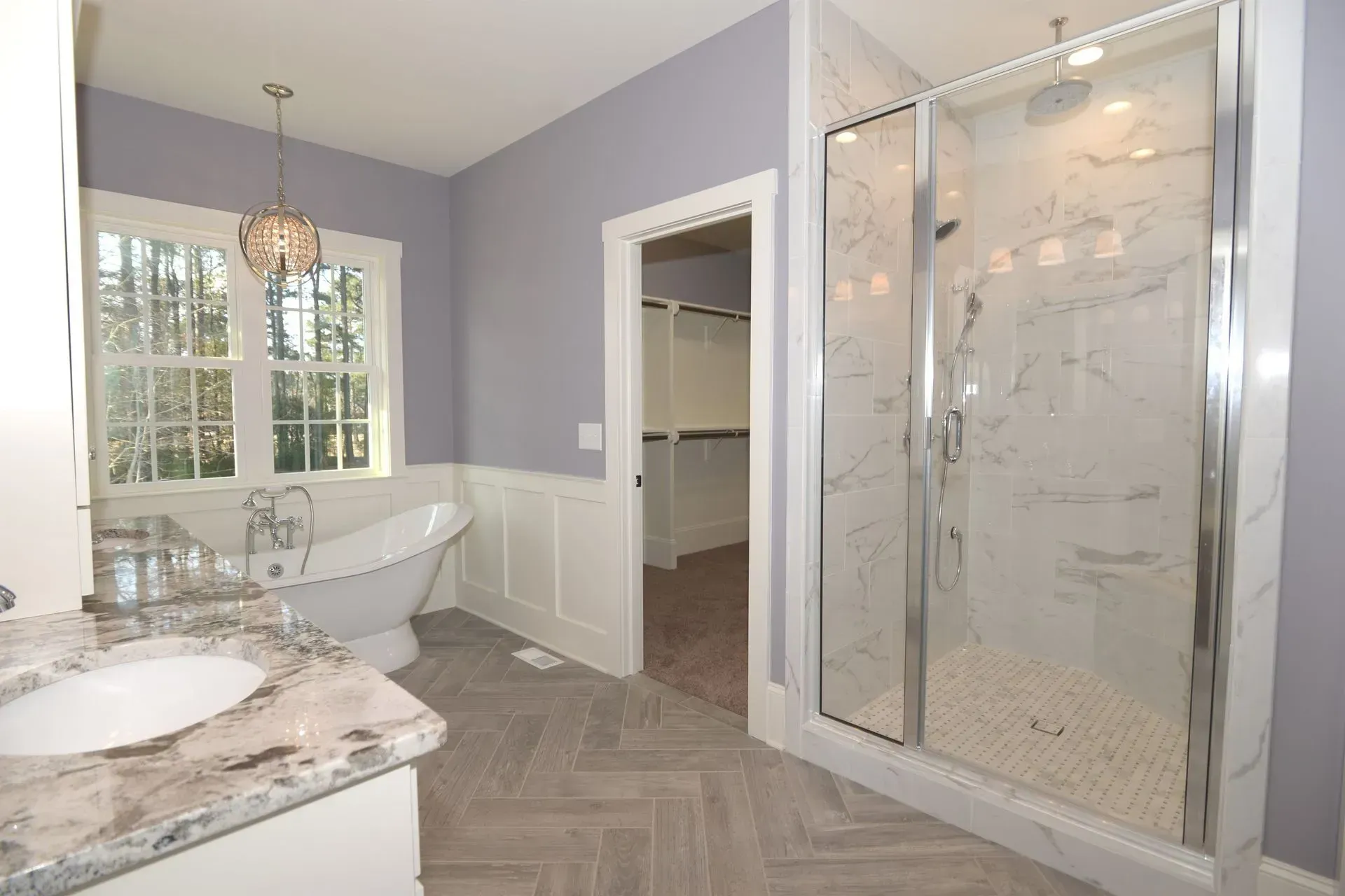 A modern bathroom with a freestanding tub, a marble shower stall, a vanity with a sink, and herringbone tile flooring.