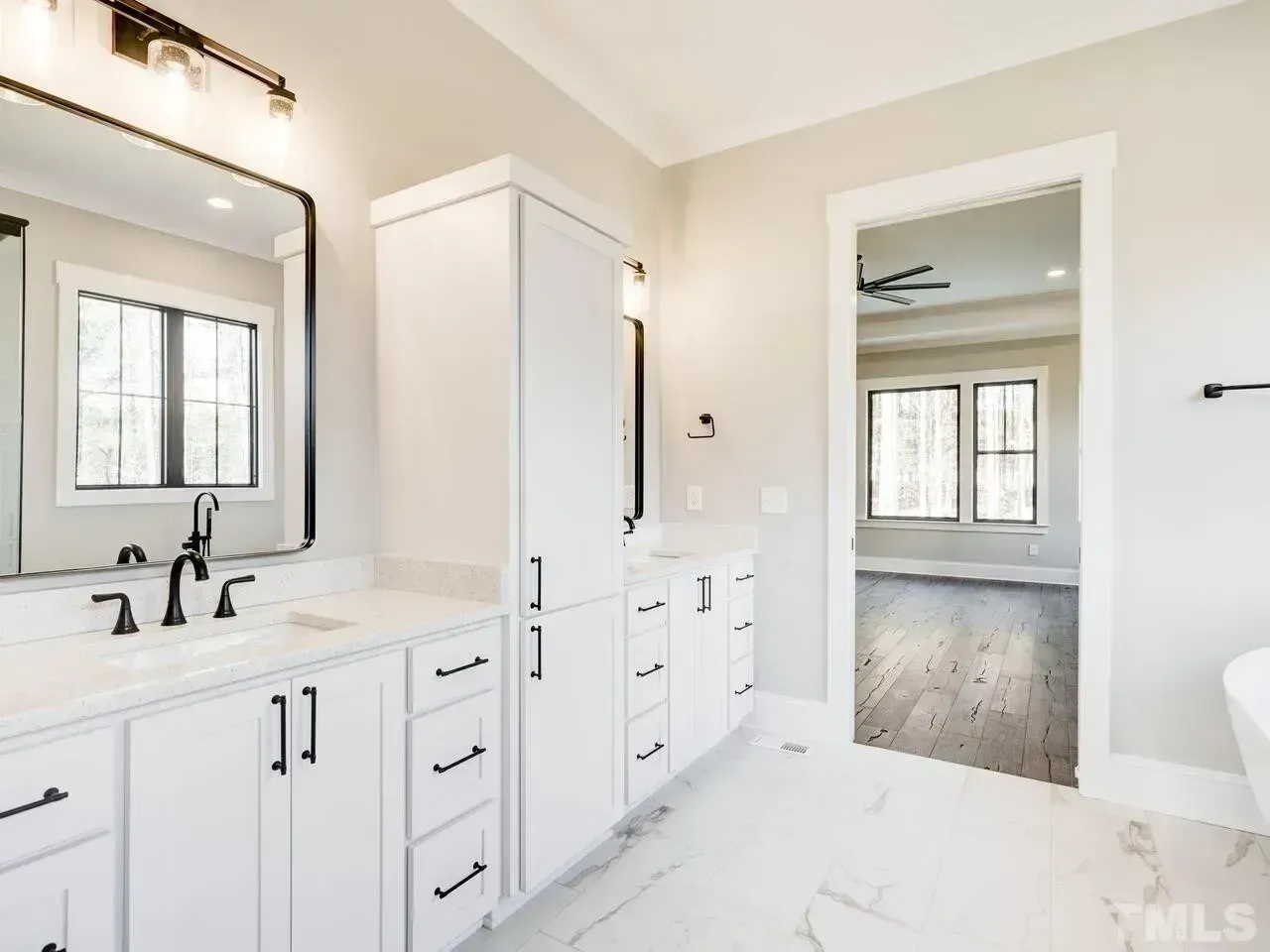 Modern white bathroom vanity with a mirror, wall lights, and a doorway opening to an adjacent room with wood floors.