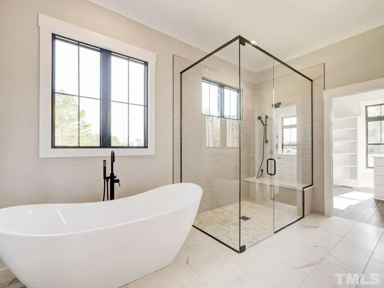 A modern bathroom featuring a white freestanding soaking tub, a glass-enclosed walk-in shower, and a large window.