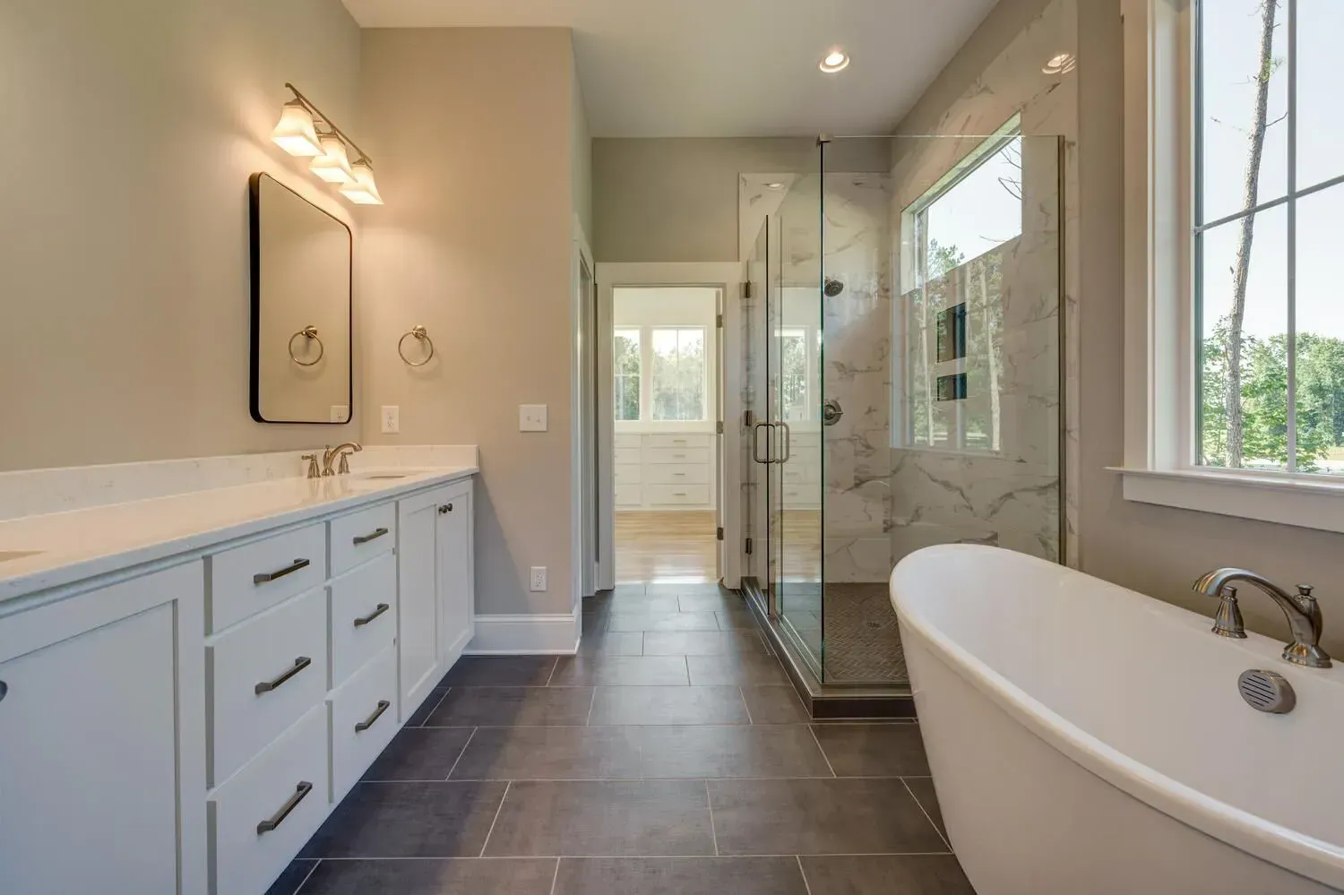 A modern bathroom featuring a white vanity with drawers, a freestanding tub, a glass-enclosed shower, and dark tile floor.