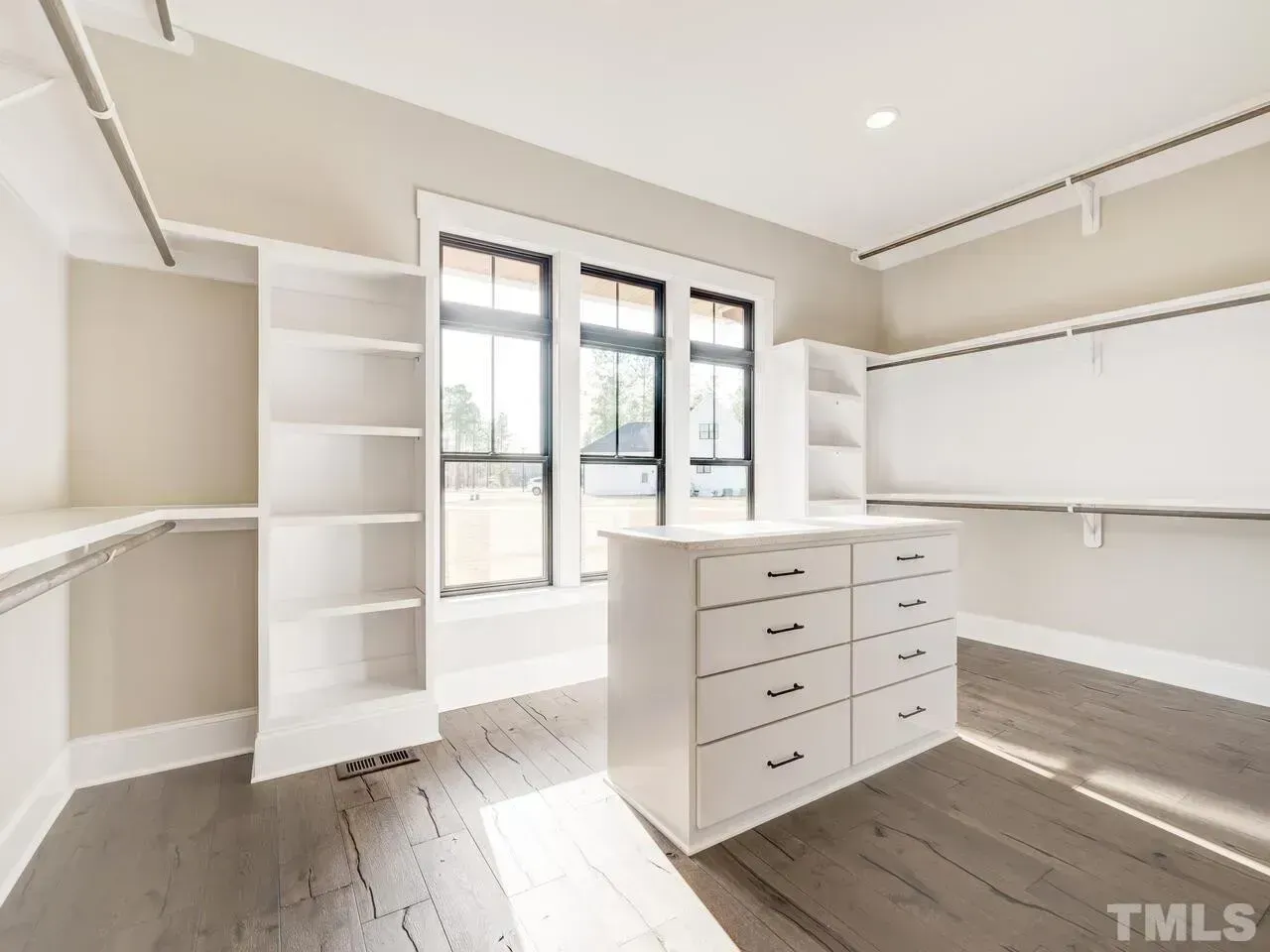 A bright, modern walk-in closet featuring white shelves, a central island with drawers, and large windows.